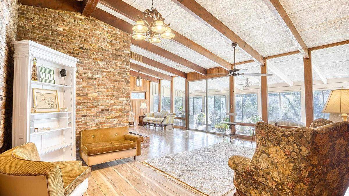 The open concept living space is brightly lit from the large number of windows and is accented by wood beams on the ceiling.