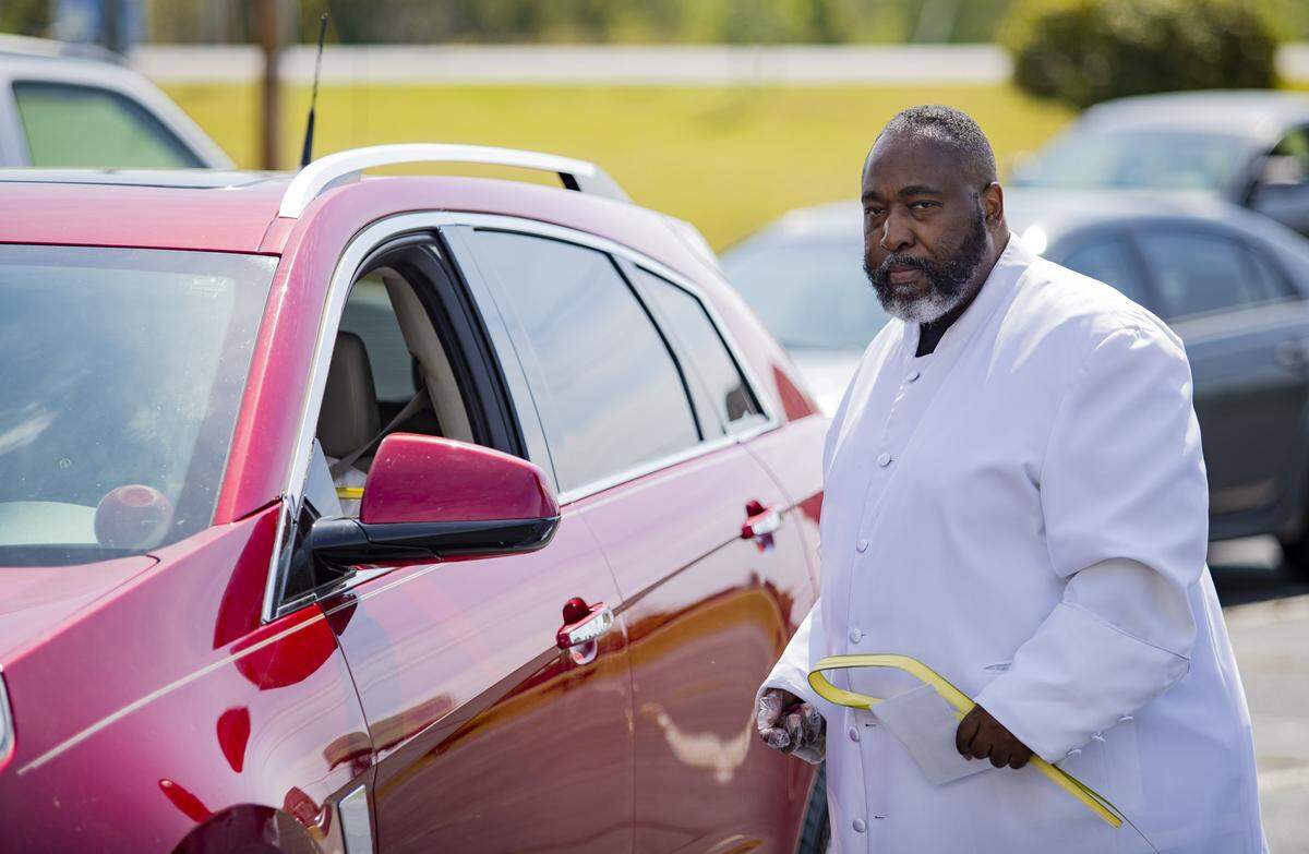 Reverend Johnathan Greene of the Saint Paul Church in Little River gives communion to one of his parishioners during a drive-through communion service on Palm Sunday, April 5, at his church in Little River.