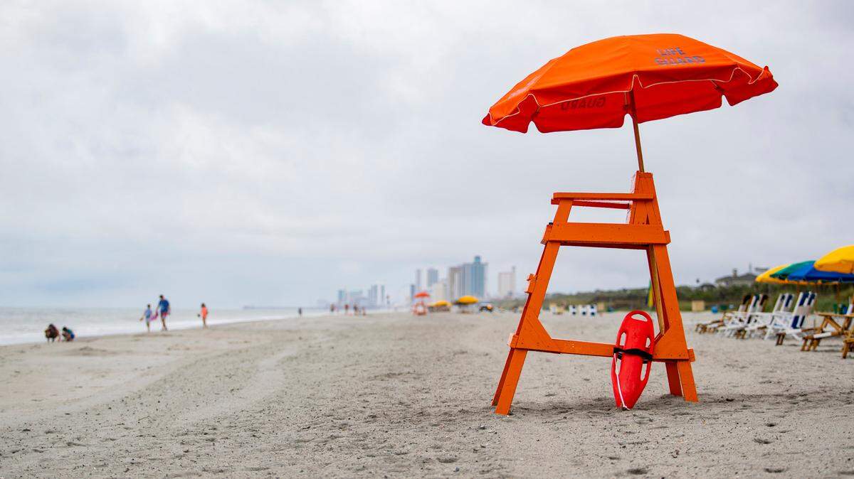 People walk along the beach near 67th Avenue North in Myrtle Beach in late June 2020 as rain falls over the Grand Strand.
