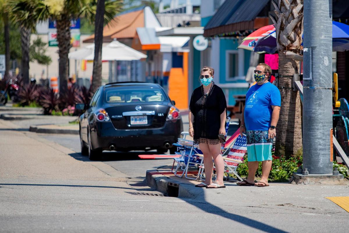 Masked pedestrians wait to cross Main Street on Tuesday afternoon in North Myrtle Beach. Coronavirus cases grew by 150 and two virus-related deaths were reported in Horry County on Tuesday, according to state health officials.