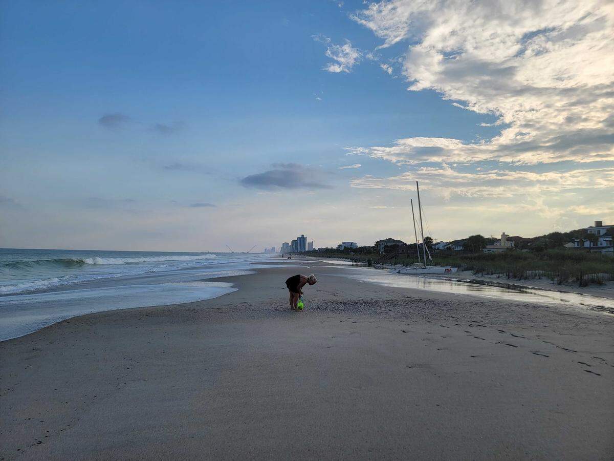 A woman looks for shells during evening high tide bolstered by Hurricane Erin, Aug. 19, 2025.