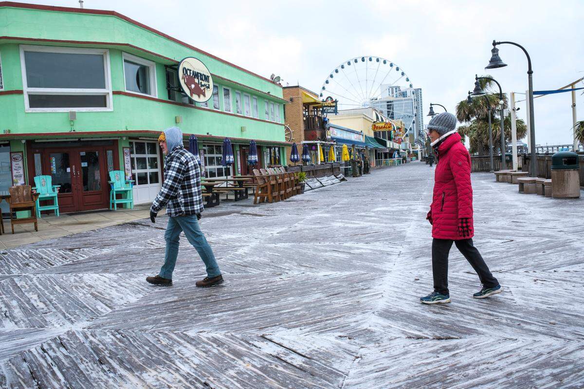 Visitors walk the Myrtle Beach Boardwalk looking for a store selling coffee on Saturday morning. A rare winter storm struck the Grand Strand area on Friday, Jan. 21st and Saturday Jan. 22, 2022 coating everything in the region with a glaze of ice. Jan. 22, 2022.
