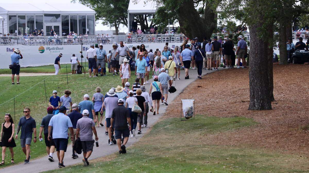 Spectators walk past the VIP seating at hole 18 towards the Dunes Golf & Beach Club’s clubhouse. Dark skies and occasional rain potentially impacted the tournament’s attendance.