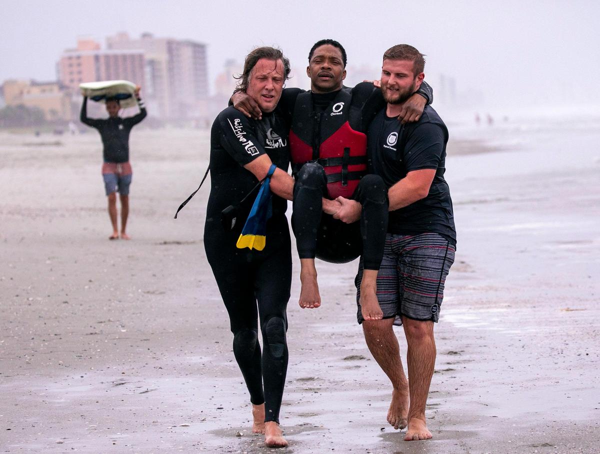 Tyler Watkins and Karl Elhers carry Ernie Johnson, a quadriplegic surfer, from the ocean after a surf session on Wednesday. Johnson will be competing in the USA Surfing adaptive Championships on June 13, 2019.