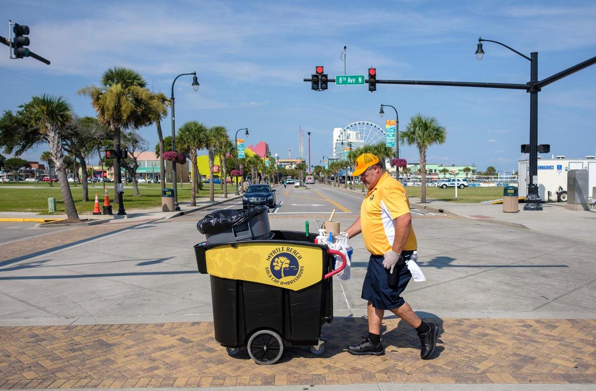 Jeremy Trendle pushes is cleaning cart across Ocean Boulevard in Myrtle Beach on Wednesday afternoon. A dozen Gold Cap Ambassadors are now patrolling the streets of Myrtle Beach cleaning up trash, providing hospitality services, and reporting issues to city officials.The pilot program started in August as a way to improve the safety and cleanliness of the tourism district. August 26, 2020.