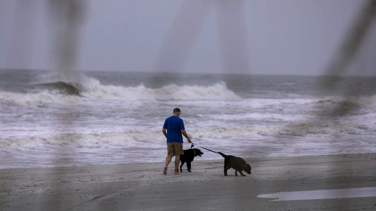 A man walks his dogs on the beach during a break between rain squalls. Thursday Sept. 04, 2019.
