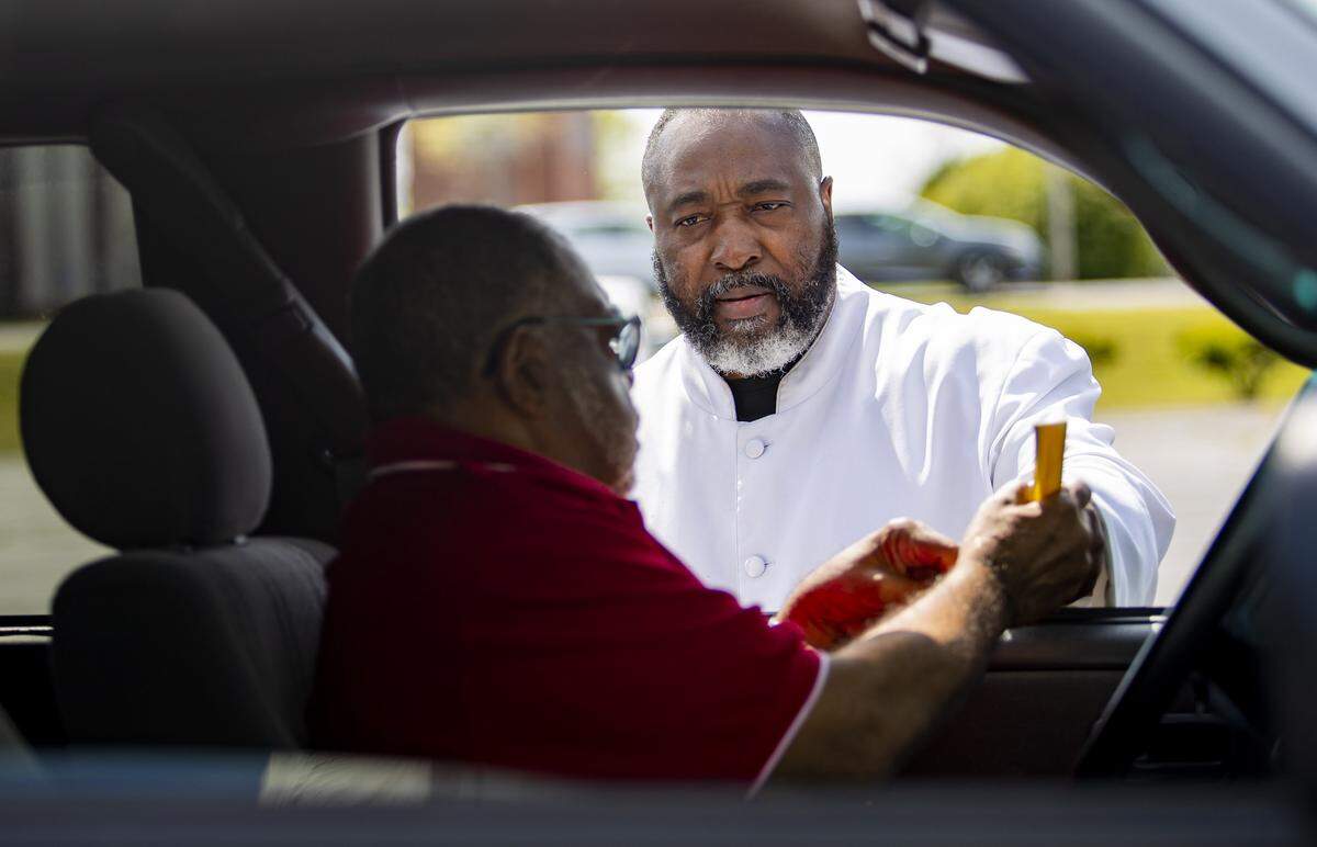 Reverend Johnathan Greene of the Saint Paul Church in Little River gives communion to one of his parishioners during a drive-through communion service on Palm Sunday, April 5, at his church in Little River.