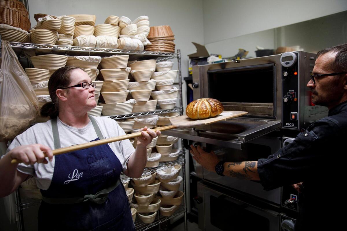 Audrey Brletich and James Levy pull sour dough bread from the oven at Leve’ Bakery. Leve’ Bakery prepares sour dough bread for their retail shop and farmers market. They prepare 50 to 60 loaves a day. Oct. 23, 2024.