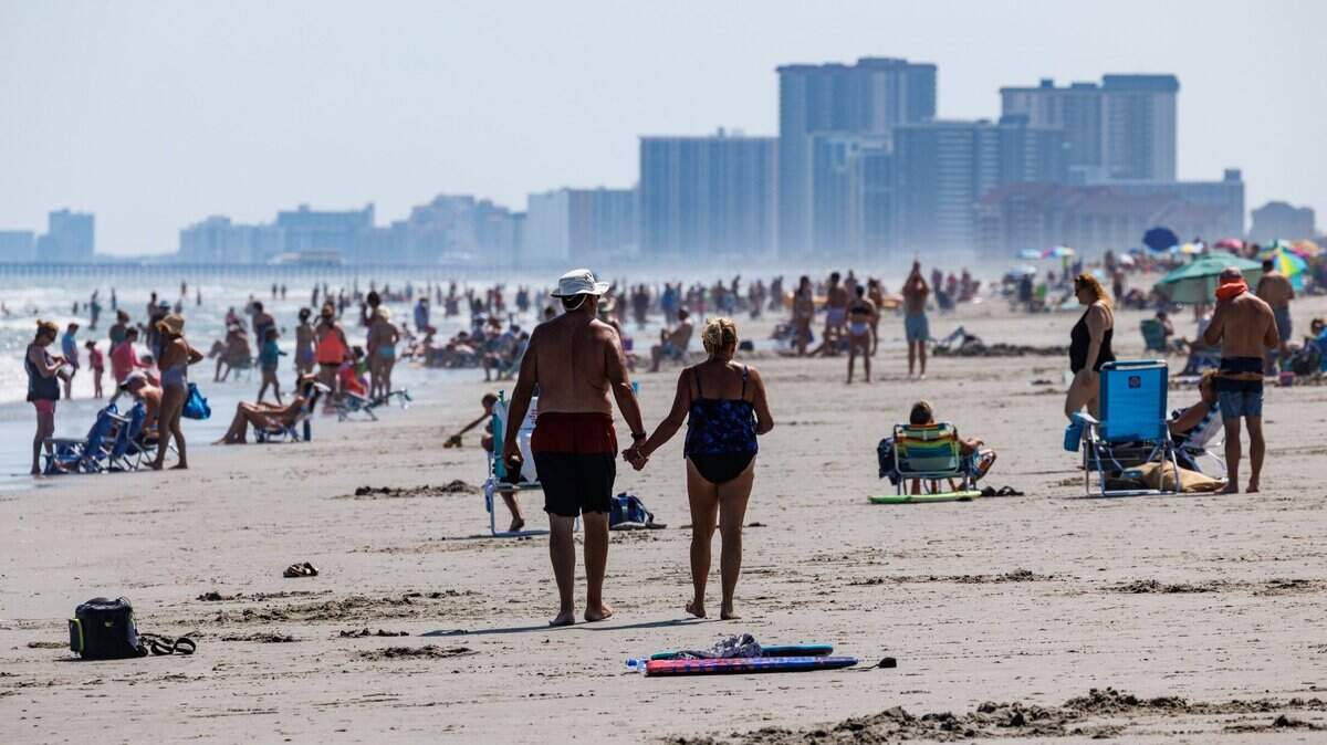 A couple strolls a crowded section of North Myrtle Beach on a hazy hot summer day. Grand Strand area beaches are packed with sunbathers despite a heat wave that has temperatures with relatively humidity climbing near 100F. June 26, 2025. 