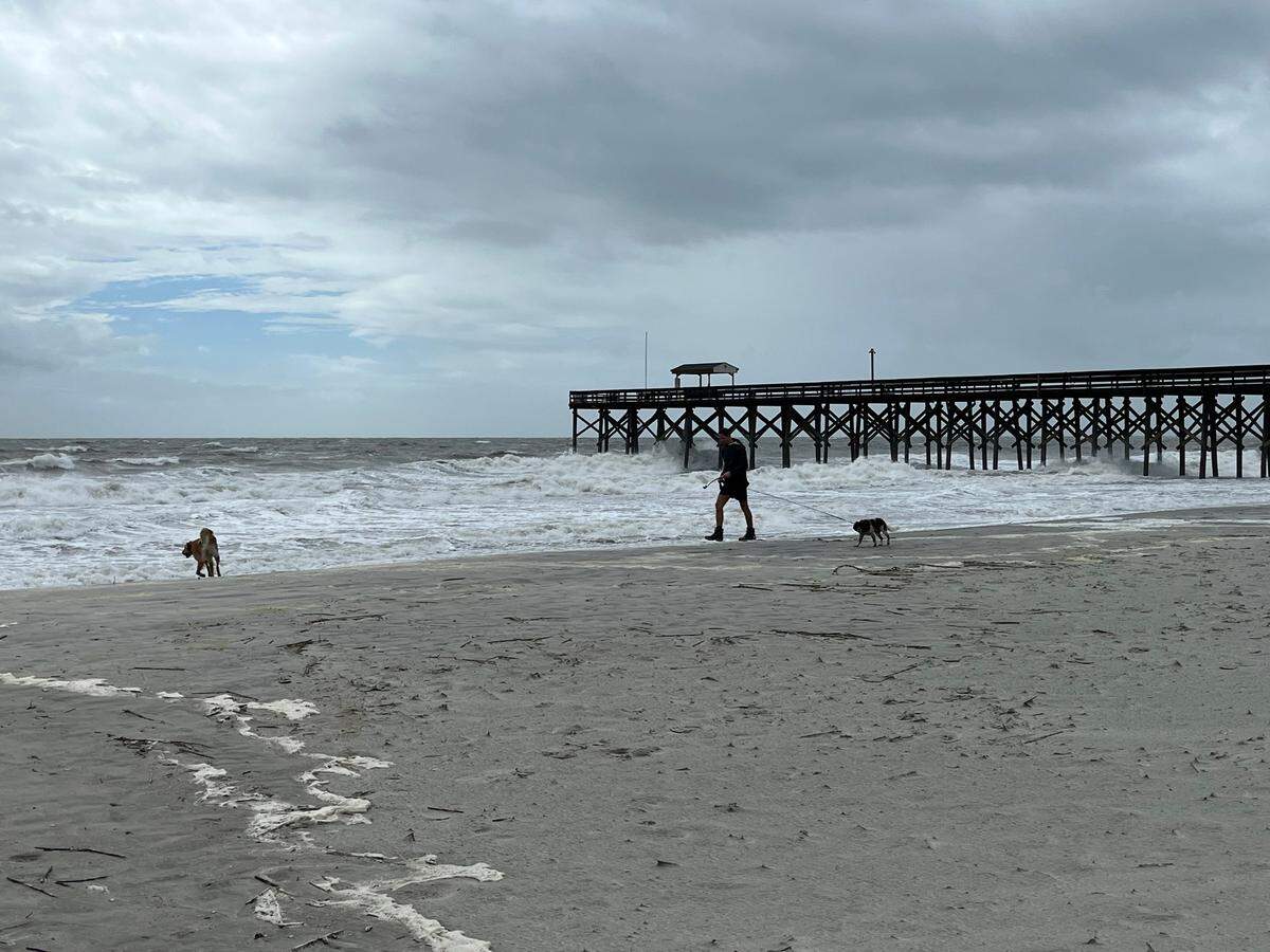Taylor Weston, 29, plays with his golden retriever Bella and cocker spaniel Birdie while walking on the beach on Pawleys Island during high tide as Tropical Storm Debby begins impacting the area Wednesday, Aug. 7, 2024.