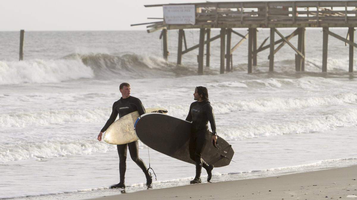 Surfers Zach Hunt (left) and Osvaldo Paredes (right) return from surfing near the Springmaid Pier that was damaged during Hurricane Matthew. Feb. 24, 2017.