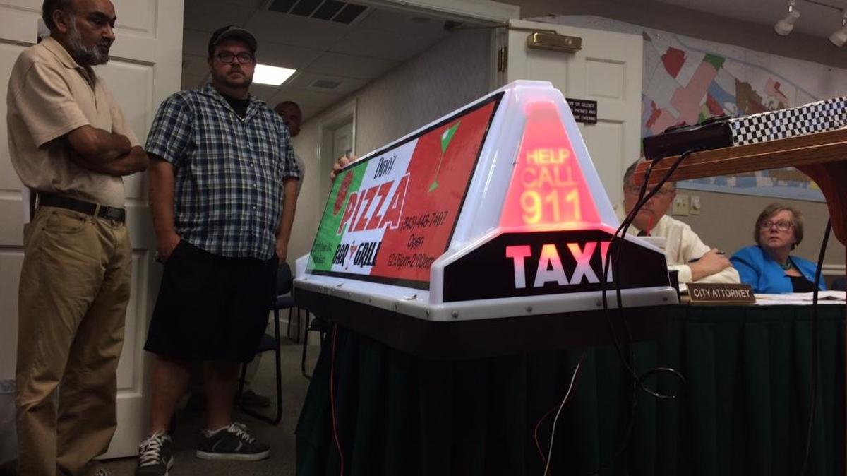Cab drivers present a sample sign at the Myrtle Beach City Council workshop on July 12. Drivers say the signs will help them generate revenue as they compete with ridesharing services.