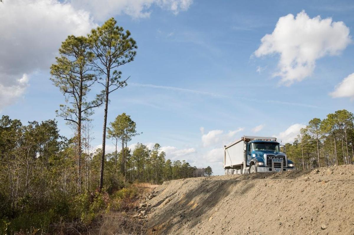 Trucks loaded with road building materials roll past wetlands off the new section of International Drive. Jan. 23, 2018.