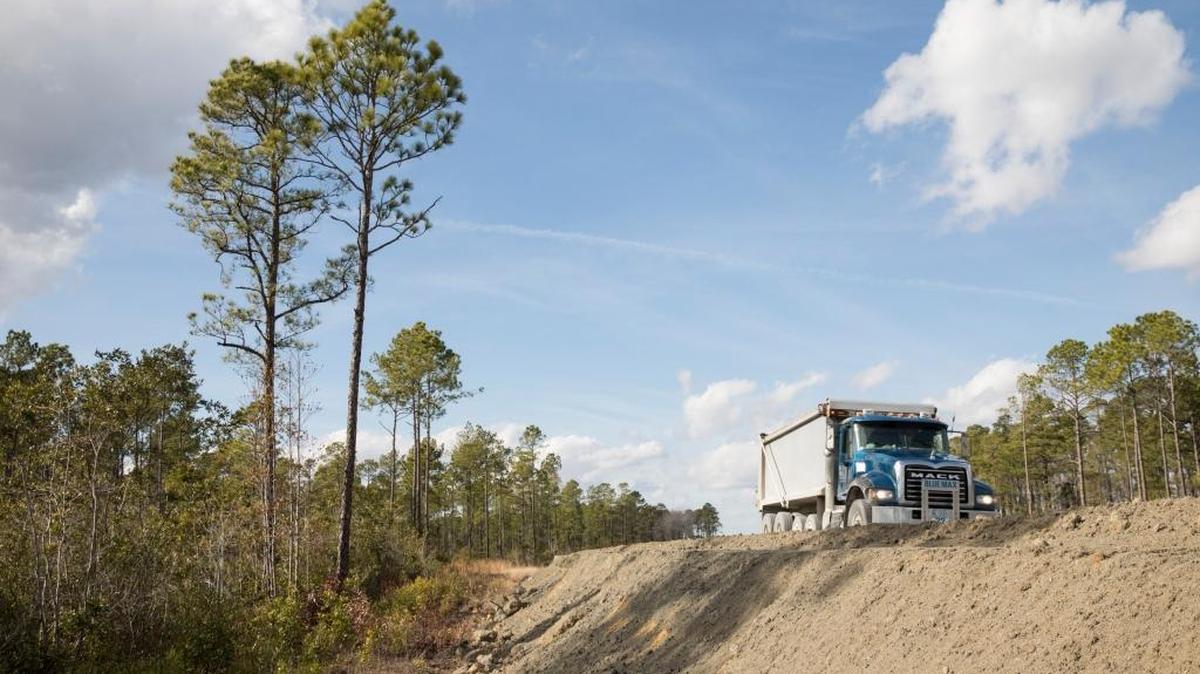 Trucks loaded with road building materials roll past wetlands off the new section of International Drive. Jan. 23, 2018.