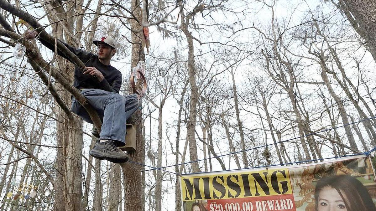 Dylan Lowrimore lights a candle in a tree during the second memorial vigil for Heather Elvis at Peachtree Landing on Friday.