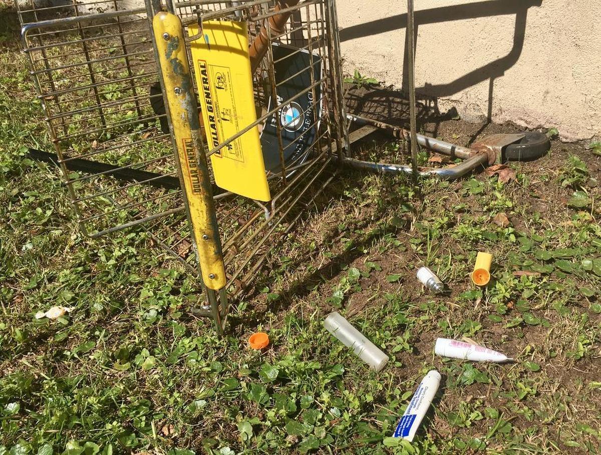 An overturned shopping cart rests by a building along 3rd Avenue North near a tube of fungus treatment and a dismantled inhaler.