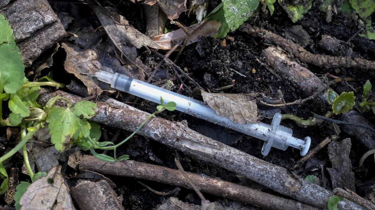 Used hypodermic needles litter the ground.