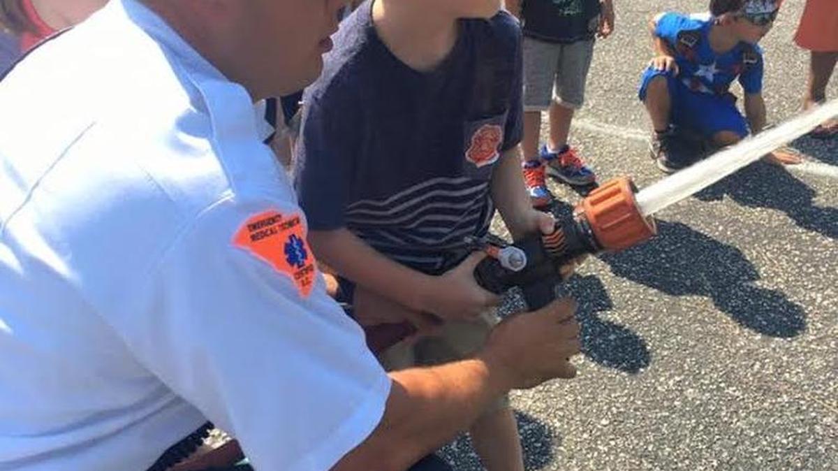 Lt. Seth Holzopfel with the Myrtle Beach Fire Department guides a child with a grip on a working fire hose, as part of educational outreach. The National Fire Protection Association’s annual Fire Prevention Week for 2016 is Oct. 9-15, with the theme “Don’t Wait – Check the Date! Replace Smoke Alarms Every 10 Years.”