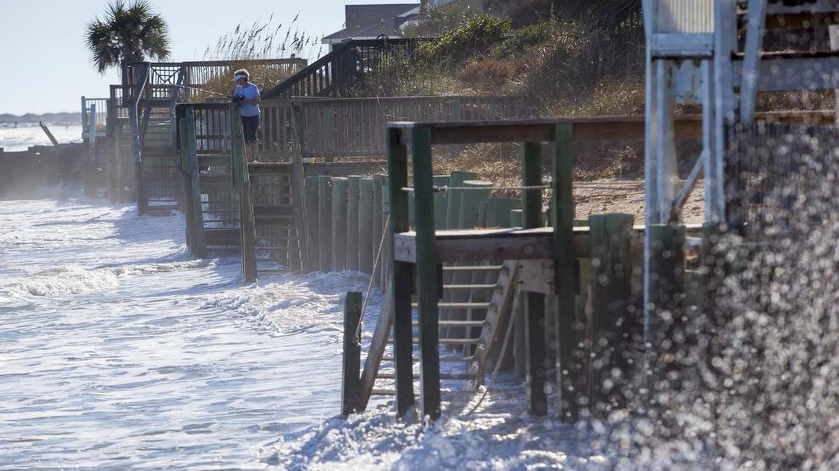 Waves crash against the sea wall as a woman fishes during a regular high tide at Garden City Point. The beaches suffered severe erosion last year.