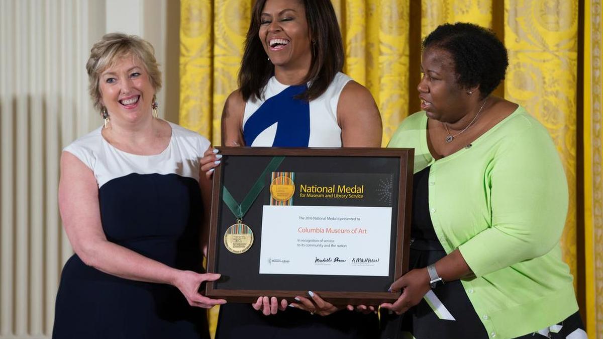 First Lady Michelle Obama laughs as she presents Karen Brosius, left, and Joyce Rose-Harris from the Columbia Museum of Art with a 2016 National Medal for Museum and Library Service award during a Wednesday ceremony at the White House. Rose-Harris, a longtime CMA patron, was invited to talk about how CMA has affected her life.