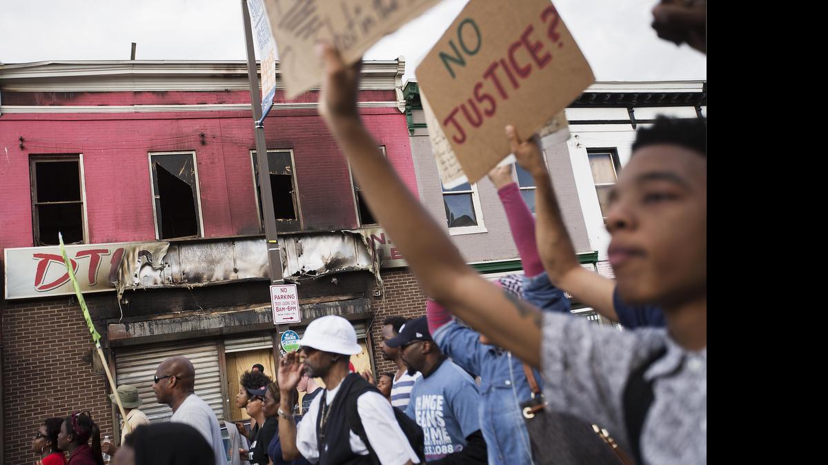 
Demonstrators march past a store damaged in the riot following Freddie Gray's funeral, Saturday, May 2, 2015, in Baltimore. Chants of "no justice, no peace, no racist police" echoed through the streets of Baltimore during the march that organizers billed as a "victory rally" a day after a prosecutor charged six officers involved in the arrest of a man who died in police custody. (AP Photo/David Goldman)

