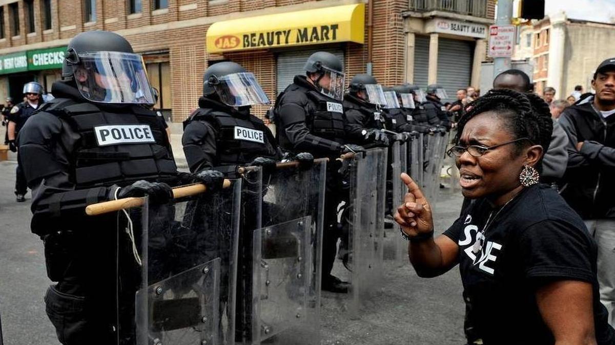 
Camille Lattimore-Weanquoi points her finger at officers lining the street where a peaceful gathering was taking place. There was a heavy police presence in some parts of the city today, including this stretch of West North Avenue, which had been the scene of looting.

