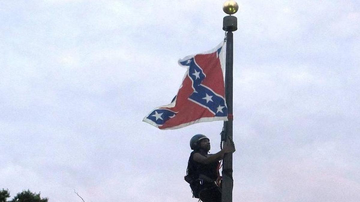 
Bree Newsome of Charlotte, N.C., climbs a flagpole to remove the Confederate battle flag at a Confederate monument in front of the Statehouse in Columbia, S.C., on Saturday, June, 27, 2015. She was taken into custody when she came down. The flag was raised again by capitol workers about 45 minutes later. | Bruce Smith AP

