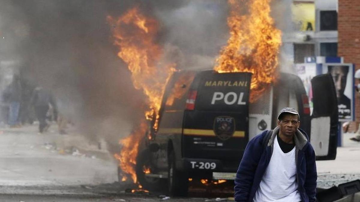 
A man walks past a burning police vehicle, Monday, April 27, 2015, during unrest following the funeral of Freddie Gray in Baltimore. Gray died from spinal injuries about a week after he was arrested and transported in a Baltimore Police Department van.

