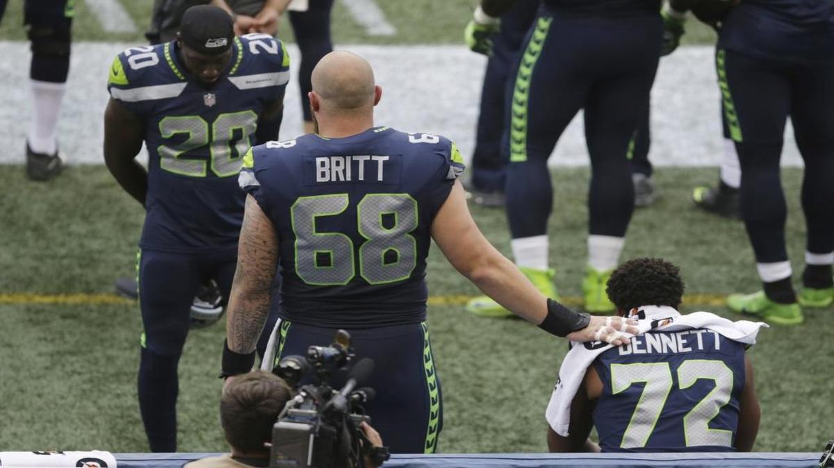 Seattle Seahawks center Justin Britt (68) and cornerback Jeremy Lane (20) stand near defensive end Michael Bennett (72) as Bennett sits on the bench during the national anthem before the team’s preseason game against the Minnesota Vikings on Friday.