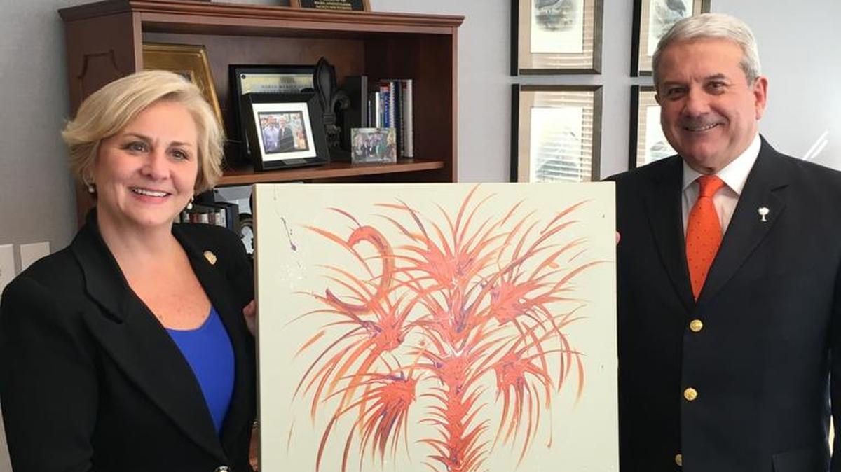 Laura and Bill Crowther hold a painting of a palmetto tree and crescent moon in Clemson colors that they recently acquired.