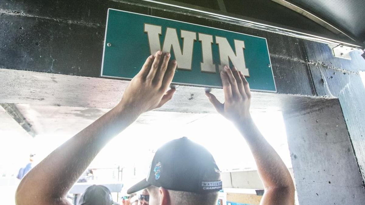 Players tap a “Win” sign on their way to the dugout in Spring Brooks Stadium last season.