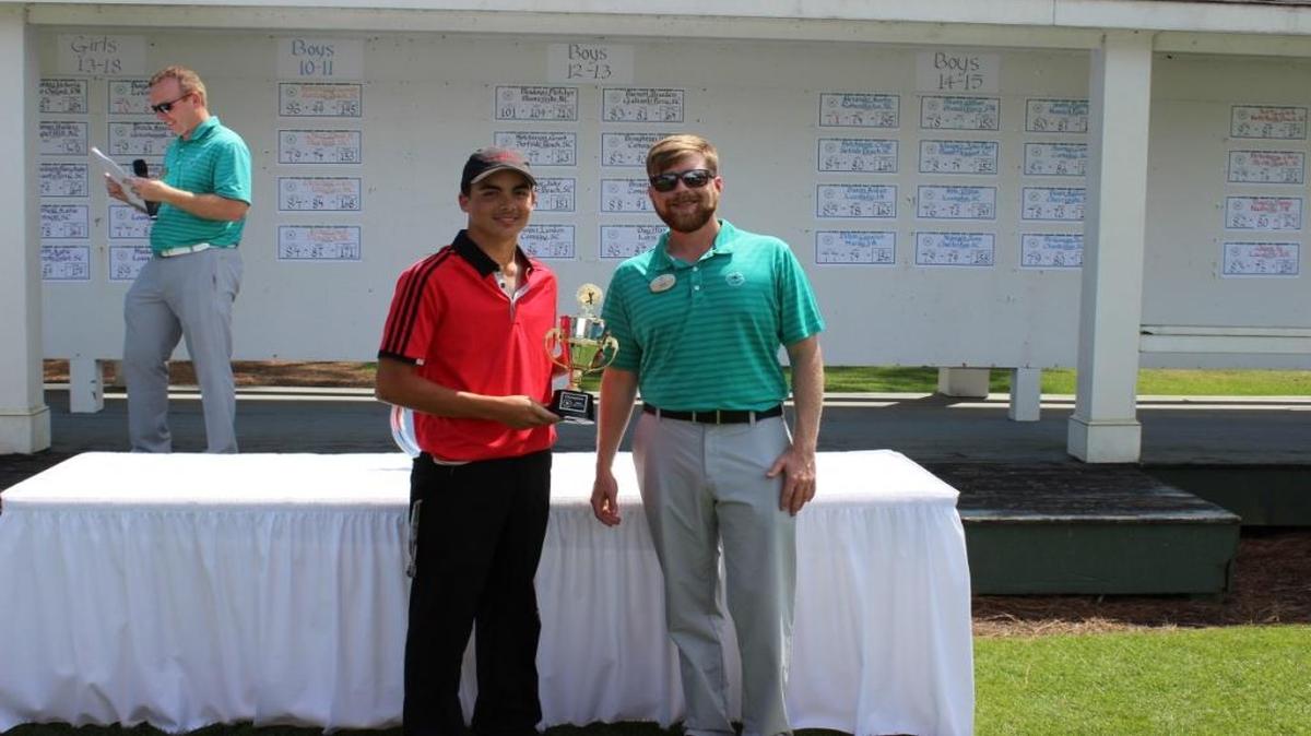 Kevin Burris accepts the winning trophy from the Myrtle Beach Junior Shootout from a staff member at Myrtle Beach National Golf Club.