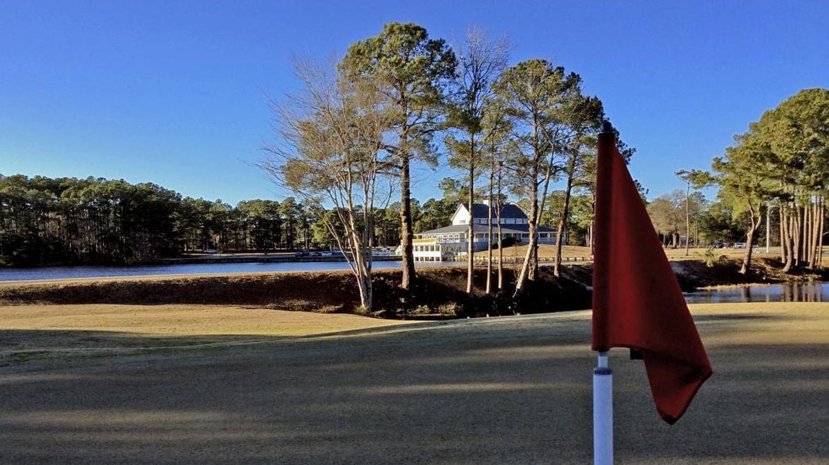 Brierwood Golf Club’s clubhouse can be seen behind a pin flag on a green.