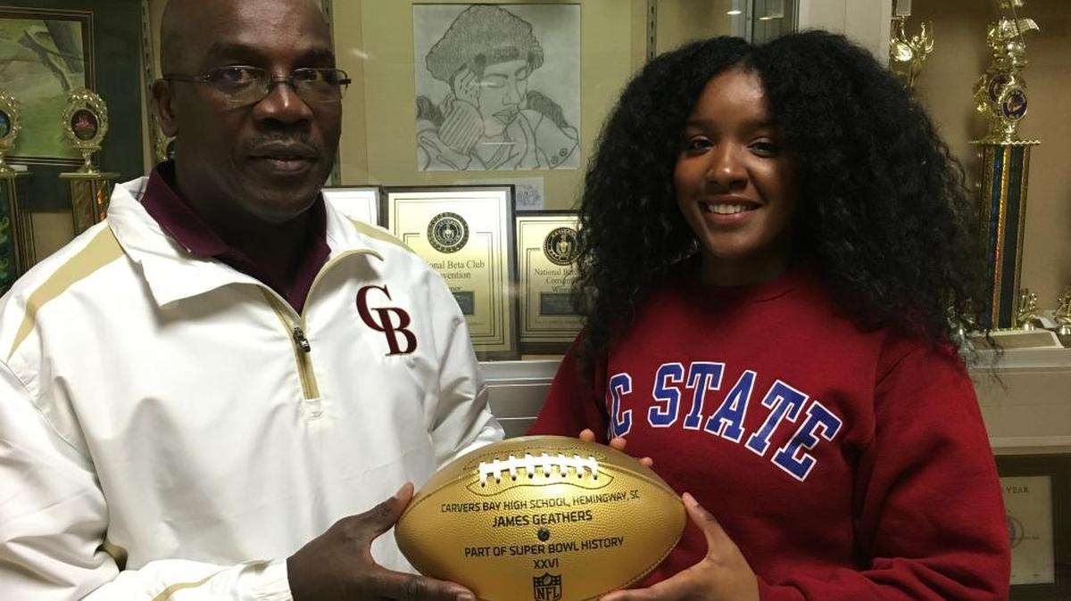 Carvers Bay principal Richard Neal accepts the Wilson Golden Football from Jasmine Geathers, daughter of Super Bowl champion Jumpy Geathers, between the boys and girls basketball games Friday night.