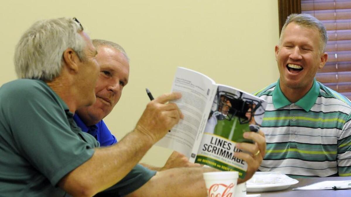 
As Loris coach Jamie Snider (second from left) looks on, Conway coach Chuck Jordan (left) gets a laugh from his former player and now coach of Myrtle Beach Mickey Wilson as they look at a photo of Wilson in his 1989 Conway uniform in the book “Lines of Scrimmage,” which is about the 1989 Conway football season.
