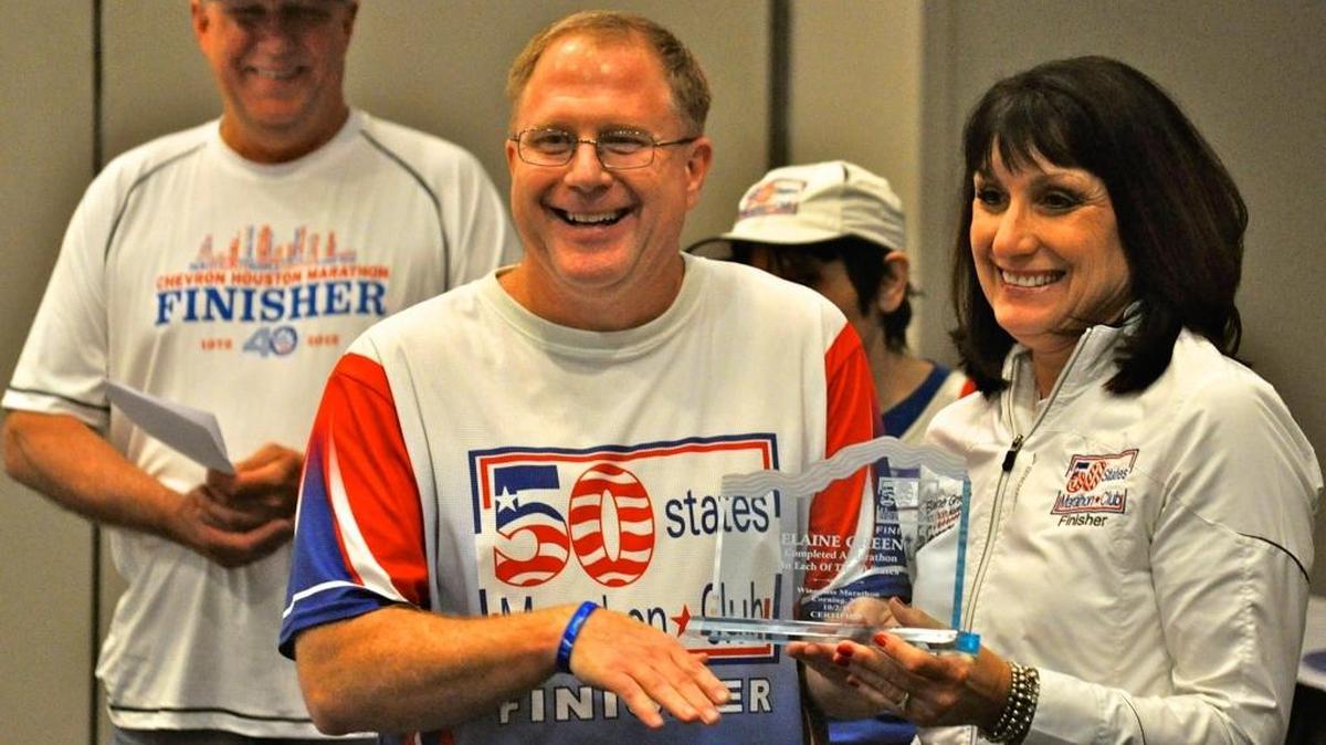 Dave Bell of the 50 State Marathon Club presents the finisher trophy to Elaine Green (Carmel, IN) for her second finish of all 50 States during a recent club event. Bell will run in the Myrtle Beach Marathon this weekend, and the club is having its quarterly meeting here.