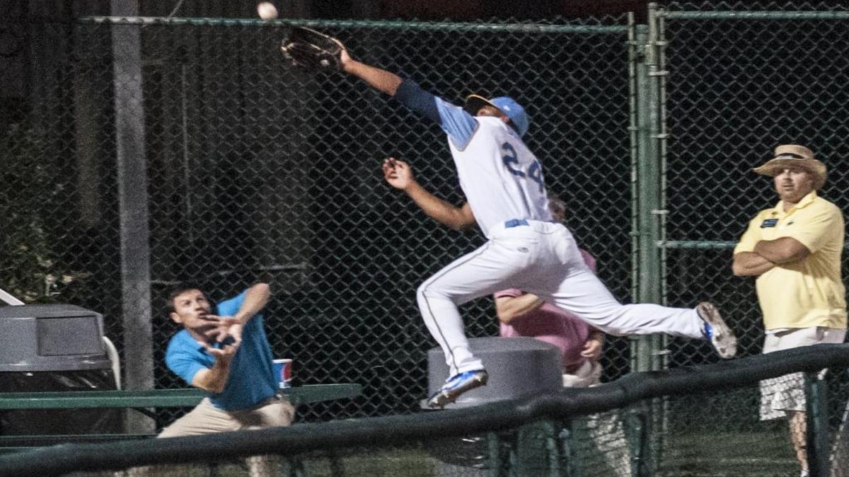 Myrtle Beach’s Charcer Burks jumps the wall into the stands to attempt to catch a foul ball in May.